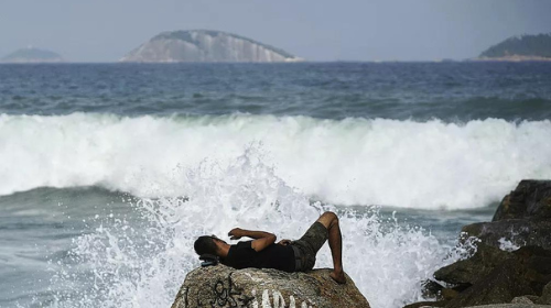 Homem deitado nas pedras da Praia do Leblon durante ressaca em maio de 2022 — Foto: Marcos Serra Lima/g1