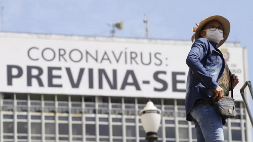 Mulher usando máscara de proteção facial passa diante de um cartaz com alerta sobre o coronavírus na região central de São Paulo. — Foto: NELSON ANTOINE/ESTADÃO CONTEÚDO